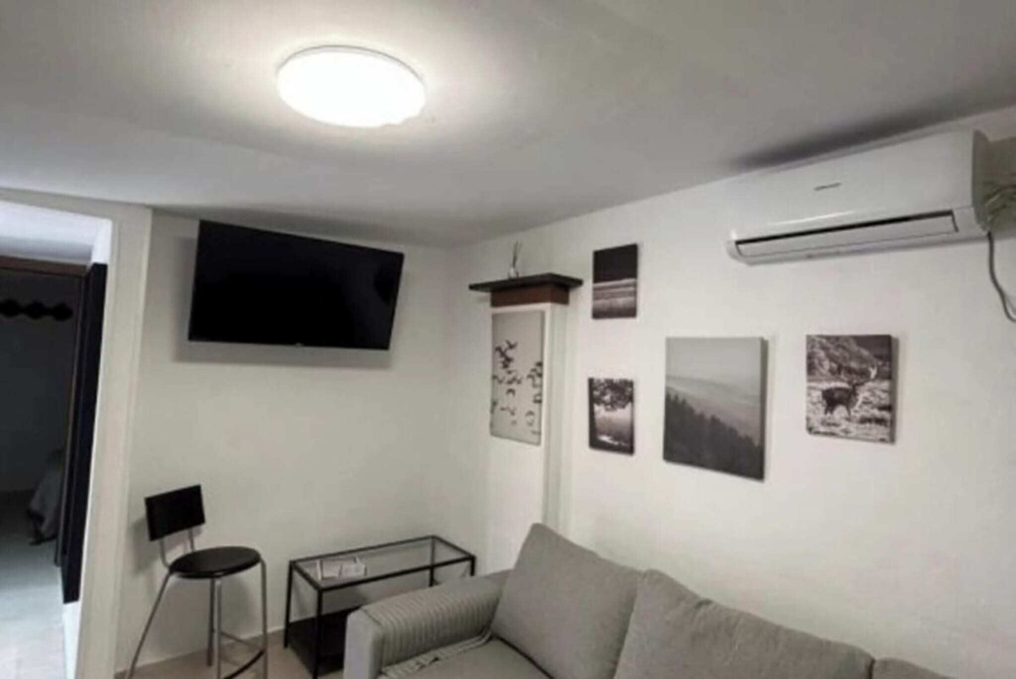 Een woonkamer met een bank, een aan de muur bevestigde televisie en een klein tafeltje.