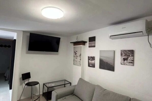 Een woonkamer met een bank, een aan de muur bevestigde televisie en een klein tafeltje.