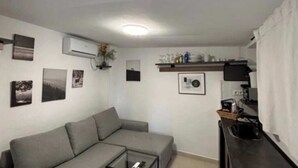 Un espace de vie comprenant un canapé, une table basse et un coin cuisine avec un comptoir et des placards.