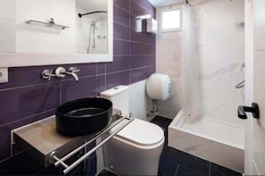 Een badkamer met toilet, wastafel, spiegel, douche en een zwarte pan op het aanrecht.