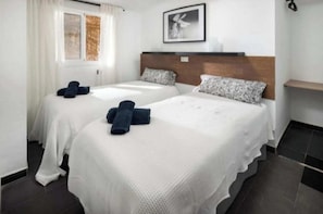 Een hotelkamer met twee bedden, een raam met gordijnen, een hoofdbord, een aan de muur hangend schilderij en een klein plankje.