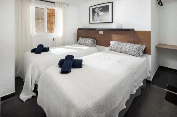 Ein Hotelzimmer mit zwei Betten, einem Fenster mit Vorhängen, einem Kopfteil, einem Wandbild und einer kleinen Ablagefläche.