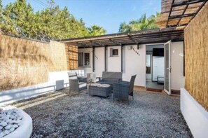A covered outdoor seating area with a gravel floor, a small table, and chairs.