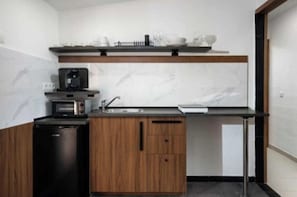 Een kleine keuken met een magnetron, koffiezetapparaat en houten kastjes.
