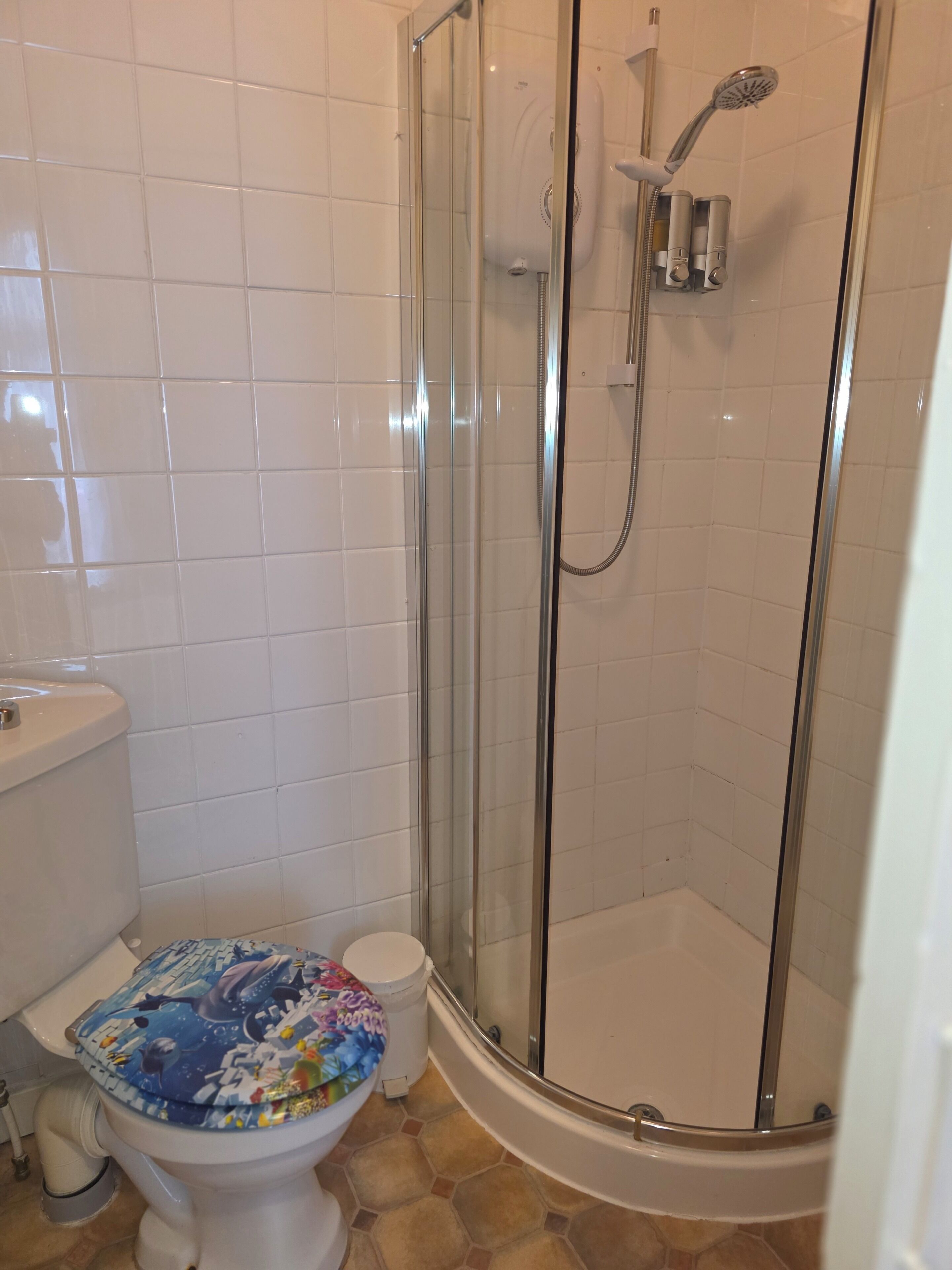 Baño con inodoro, ducha y paredes de azulejos.