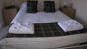 A neatly made bed with a plaid blanket, two pillows, and a white duvet. There are two bedside tables with lamps and a small drawer. - Achnabobane Farmhouse (Spean Bridge)