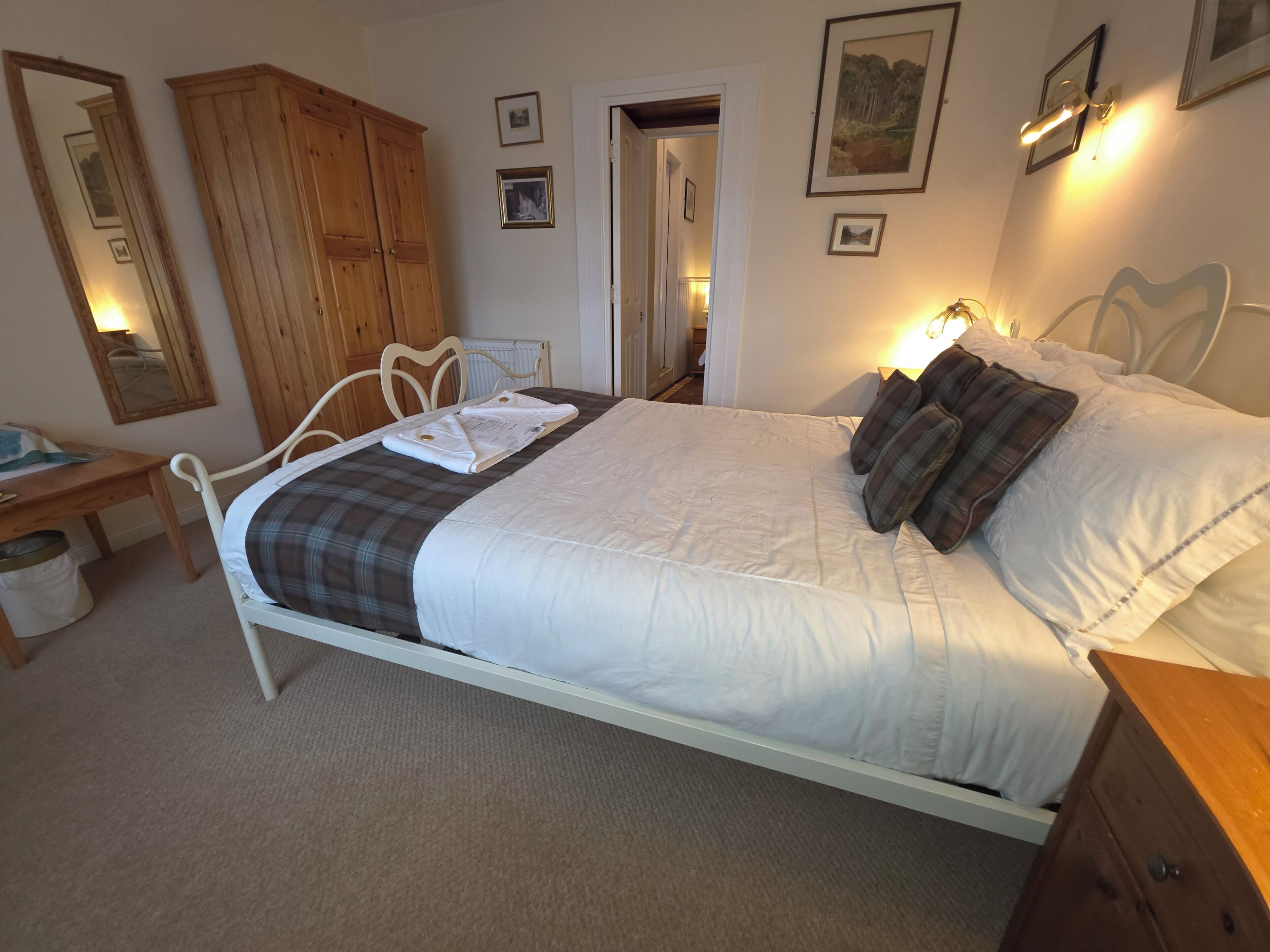 A bedroom with a bed, a wooden wardrobe, a desk, and a chair.