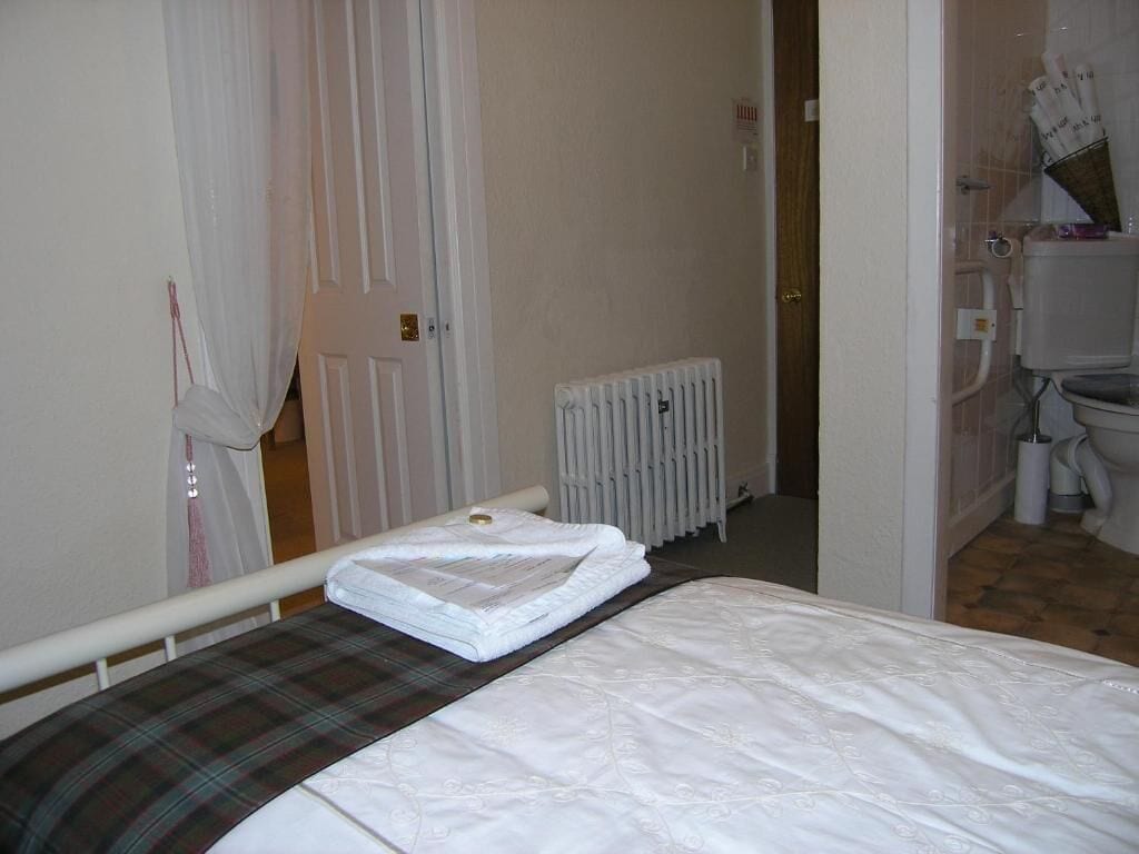 Habitación de hotel con cama, un radiador y un baño visible a través de una puerta abierta.