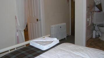 Habitación de hotel con cama, un radiador y un baño visible a través de una puerta abierta.