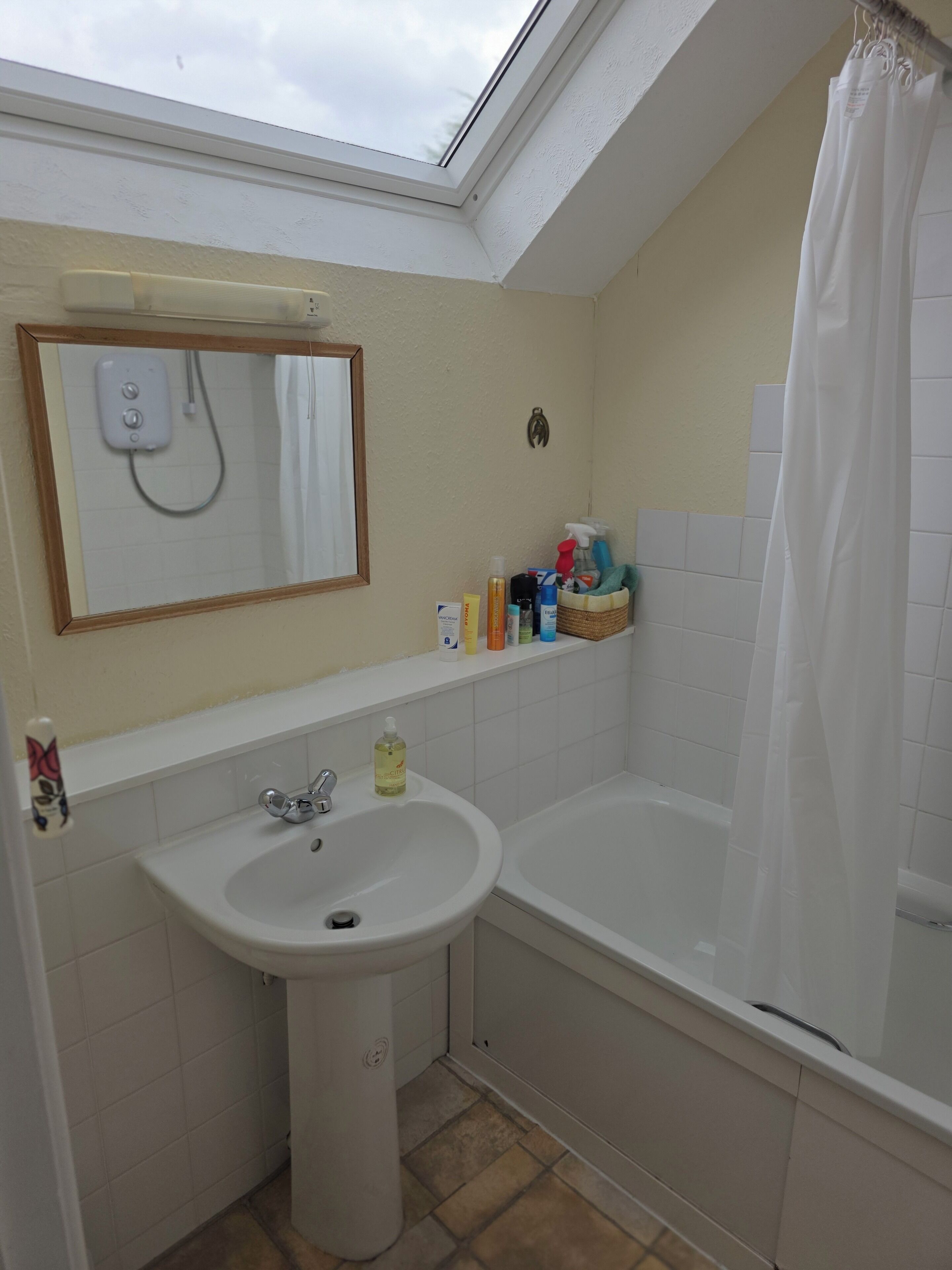 A bathroom with a skylight, a sink, a bathtub, and a shower curtain.