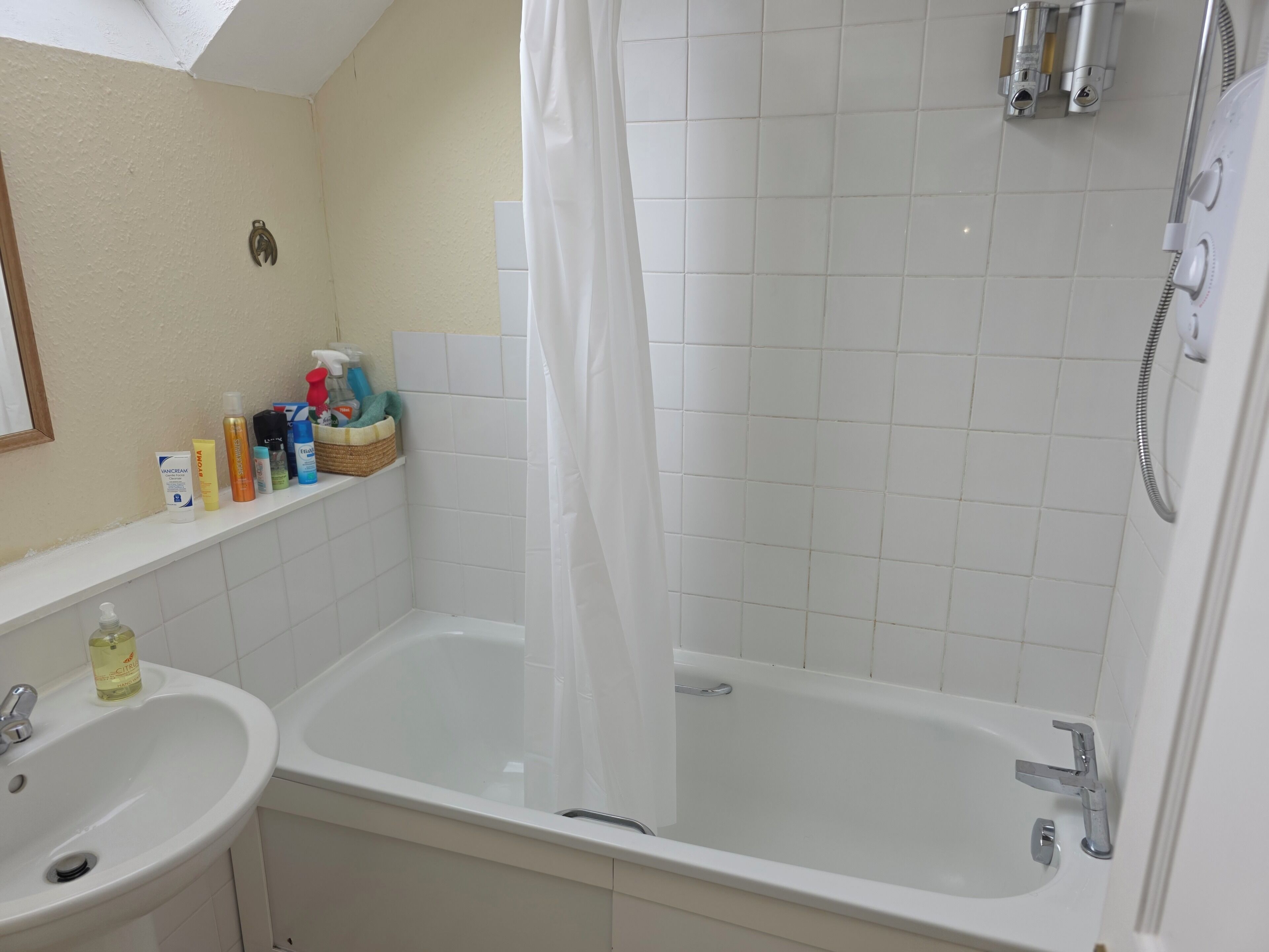 A bathroom with a bathtub, a shower, a sink, and a shelf with toiletries.