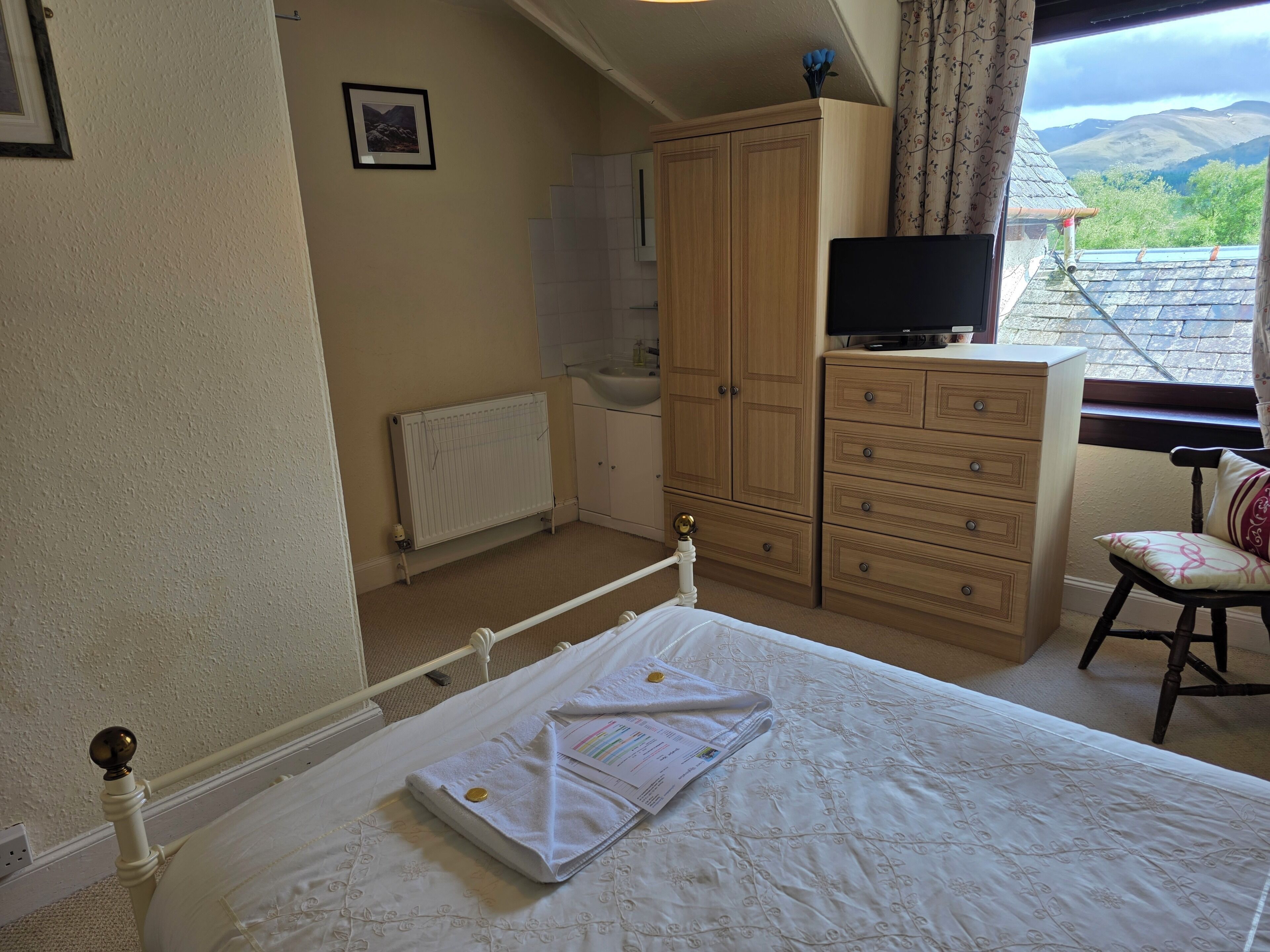 Une chambre à coucher comprenant un lit, une armoire, un téléviseur et une fenêtre donnant sur l’extérieur.