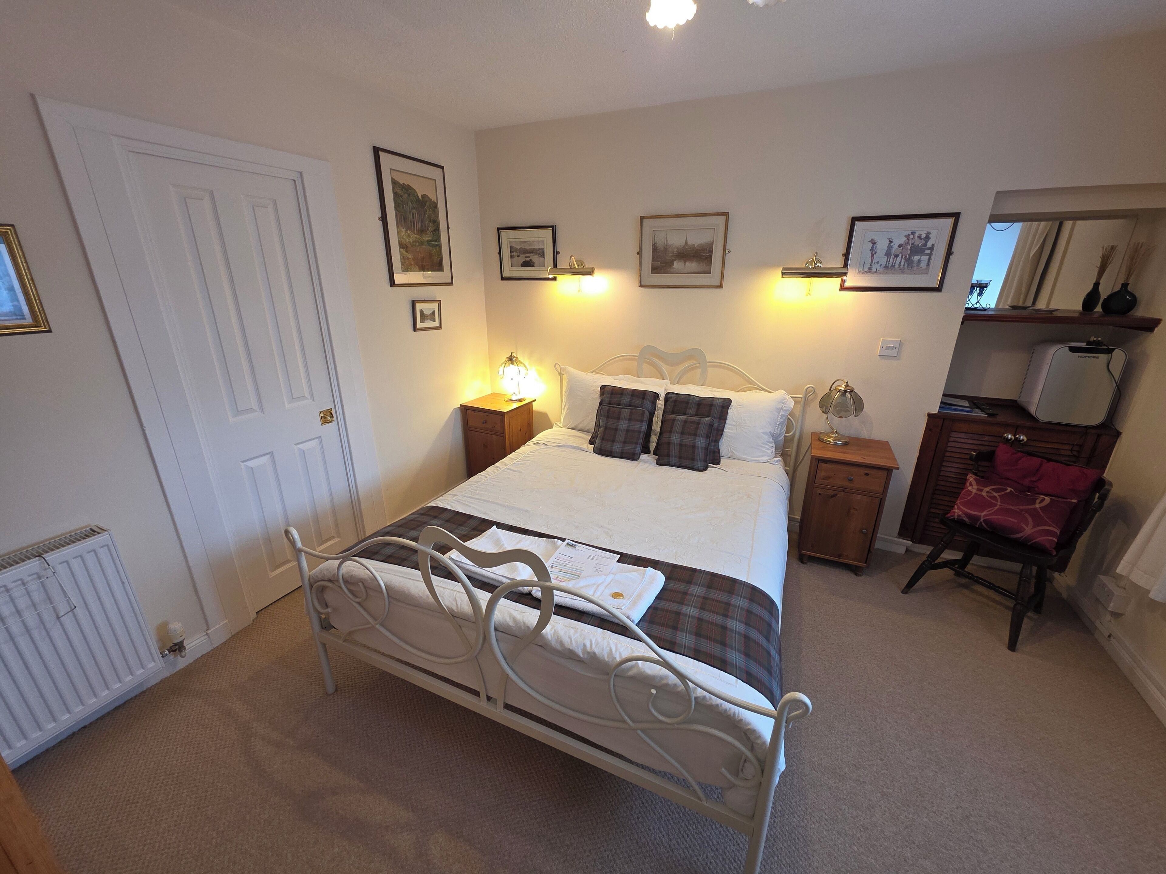 A bedroom with a bed, bedside tables, a radiator, and framed pictures on the wall.
