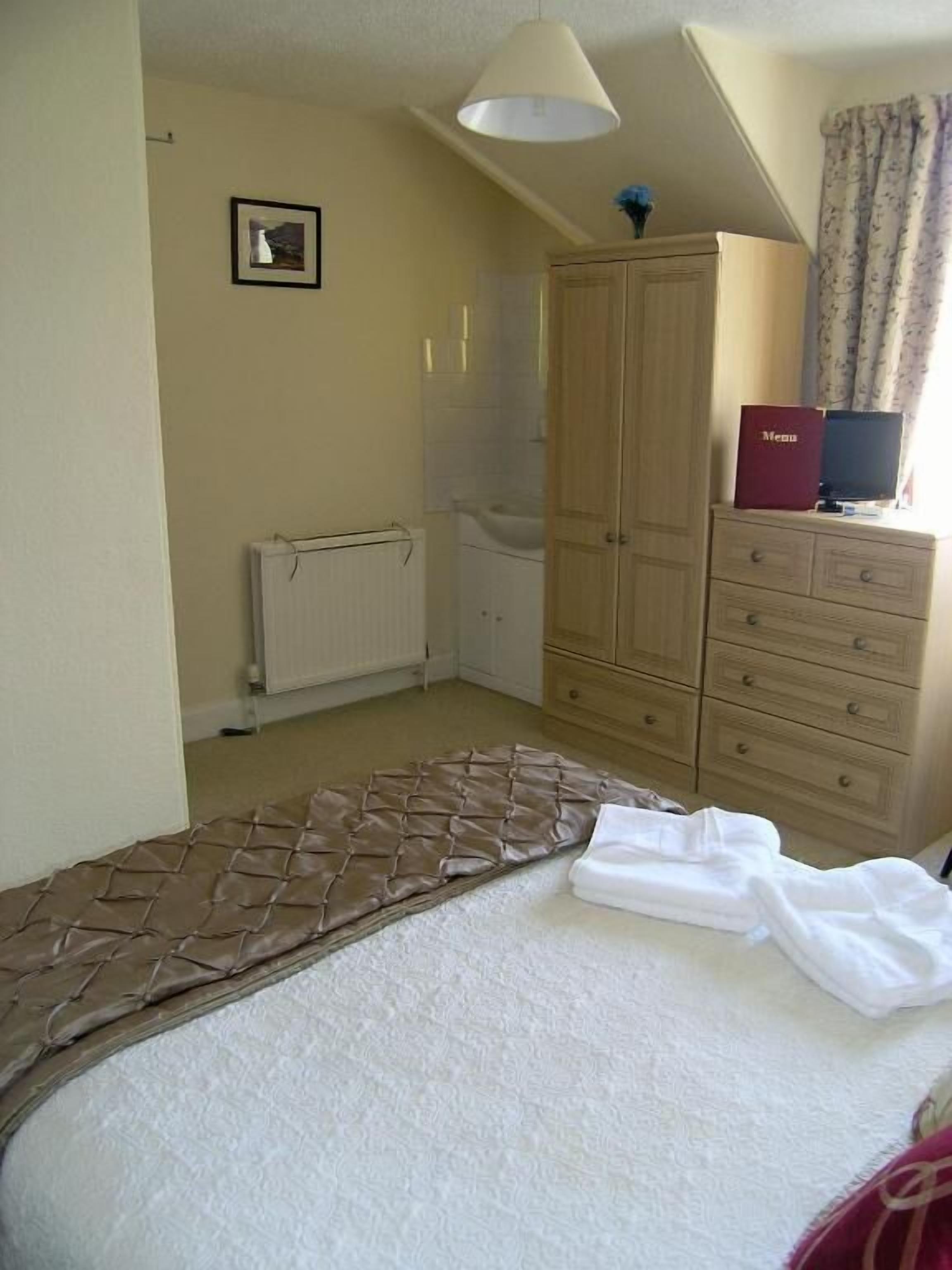 Un dormitorio con cama, armario de madera, radiador y ventana con cortinas.