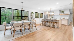 Una cocina moderna con una isla central, ventanas amplias y un comedor con una mesa redonda y sillas.