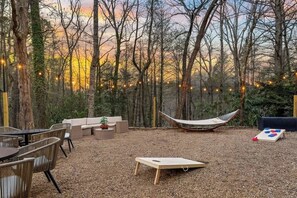 An outdoor seating area with a hammock, a wooden board game, and string lights. - Hidden Speakeasy • Hot Tub • Sauna • Private Woods (Gatlinburg)