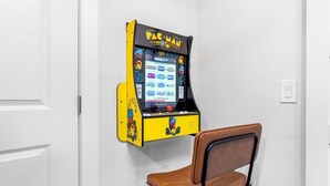Una máquina arcade de Pac-Man en una esquina con una silla marrón delante.