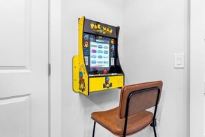 Ein Pac-Man-Spielautomat steht in einer Ecke, davor ein brauner Sessel.