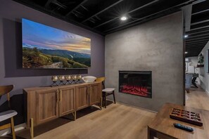 A modern living room with a large flat-screen TV, a fireplace, and a wooden cabinet. - Hidden Speakeasy • Hot Tub • Sauna • Private Woods (Gatlinburg)