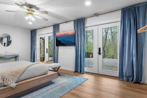 Ein Schlafzimmer mit Bett, Deckenventilator, Fernseher und einer Schiebetür, die auf einen Balkon führt.