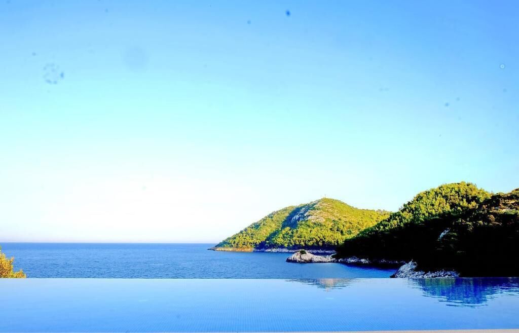 Un paisaje costero con cielo despejado, mar tranquilo y colinas verdes.