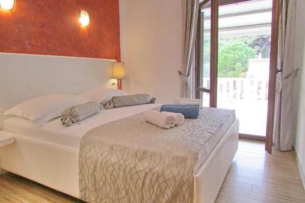 A hotel room with a bed, a nightstand, a lamp, and a view of the outside. - Villa Mirosa (Mljet)