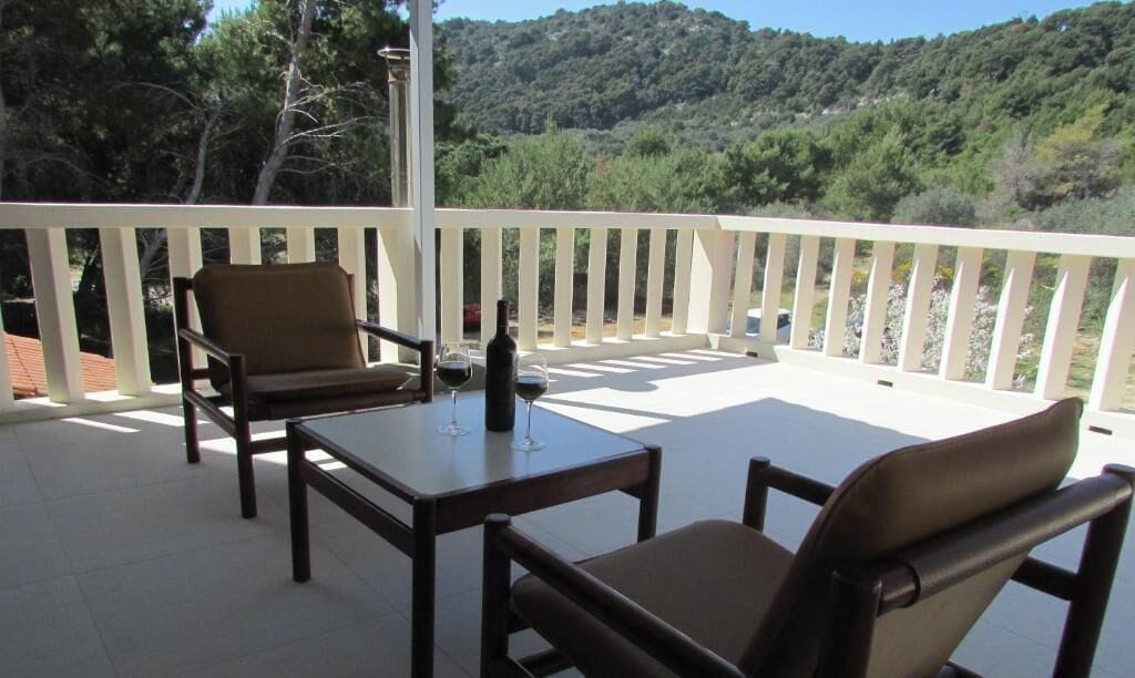 Ein Balkon mit zwei Stühlen, einem Tisch, einer Flasche und einem Weinglas.