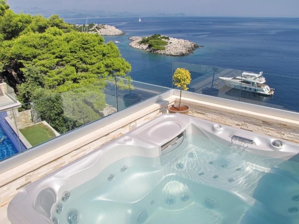 A hot tub with a glass balustrade overlooking a body of water and a yacht.