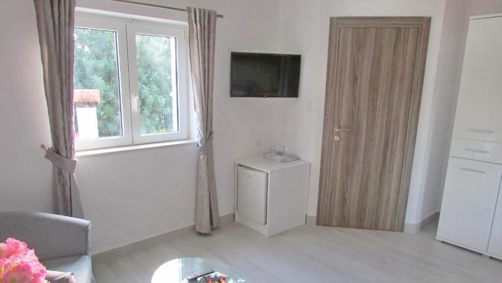A room with a window, a television, a small white cabinet, and a wardrobe.