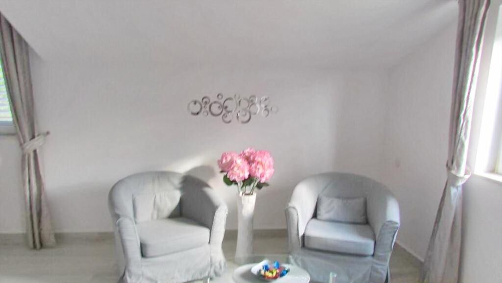 A room with two grey armchairs, a small table with a vase of pink flowers, and a decorative wall piece.