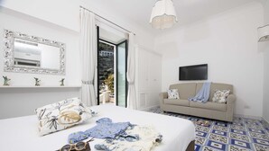 Une chambre avec un grand lit, un canapé, une télévision et un balcon avec des rideaux.