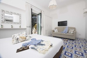 A bedroom with a large bed, a sofa, a TV, and a balcony with curtains. - AMORE RENTALS - Villa Costa Incantata with Sea View and Jacuzzi (Amalfi)