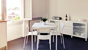 A small dining area with a white table and chairs, a radiator, a potted plant, a wine bottle, and a cabinet with dishes. - Maison Le Panche - Careggi - Loft - double exposure - on-street parking  (Firenze)