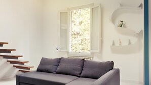 A modern living room with a grey sectional sofa, a white staircase, and a window with a view of trees. - Maison Le Panche - Careggi - Loft - double exposure - on-street parking  (Firenze)