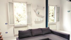 A modern living room with a grey sectional sofa, white walls, and large windows with shutters. - Maison Le Panche - Careggi - Loft - double exposure - on-street parking  (Firenze)