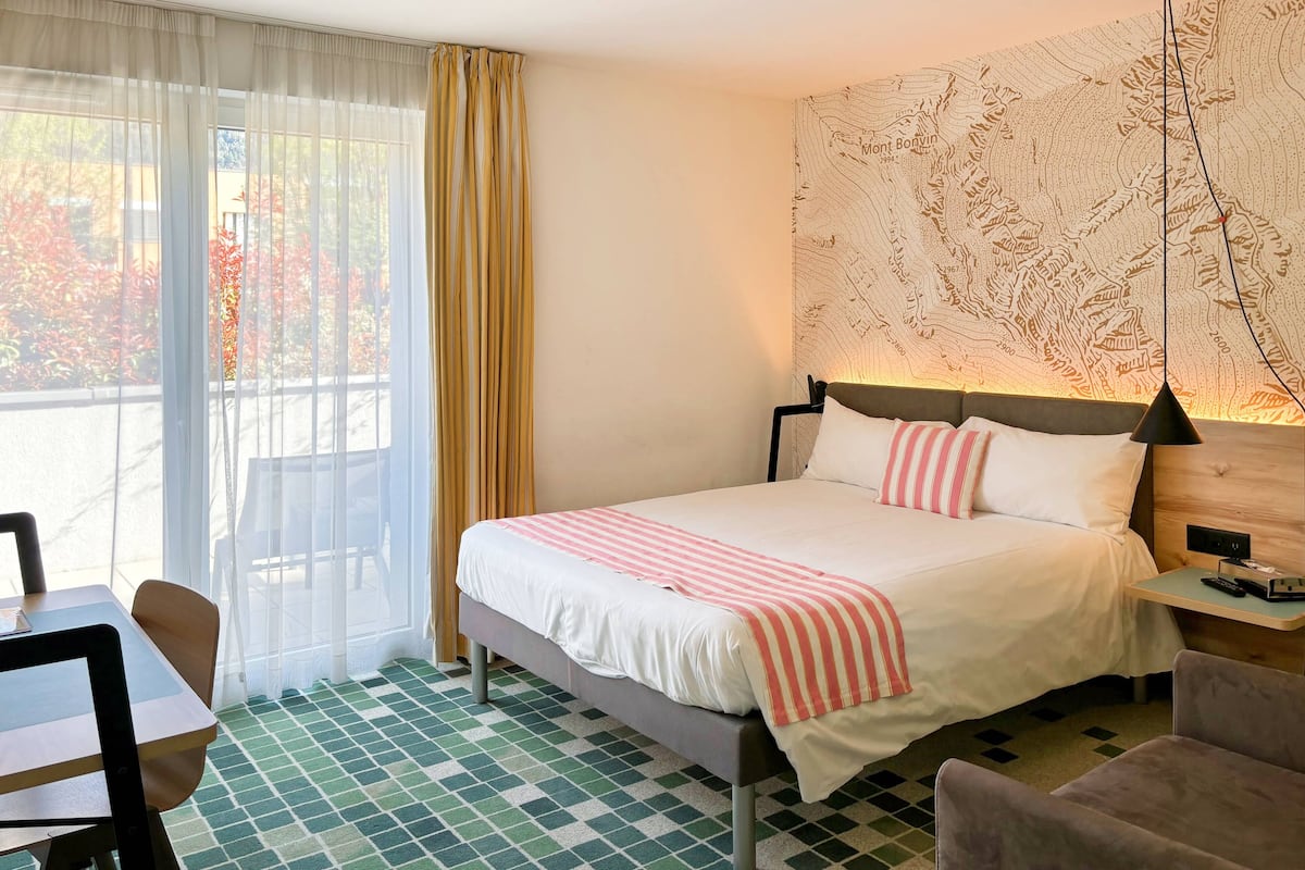 Habitación de hotel con cama, escritorio, silla, un mural de mapa y vistas al exterior.