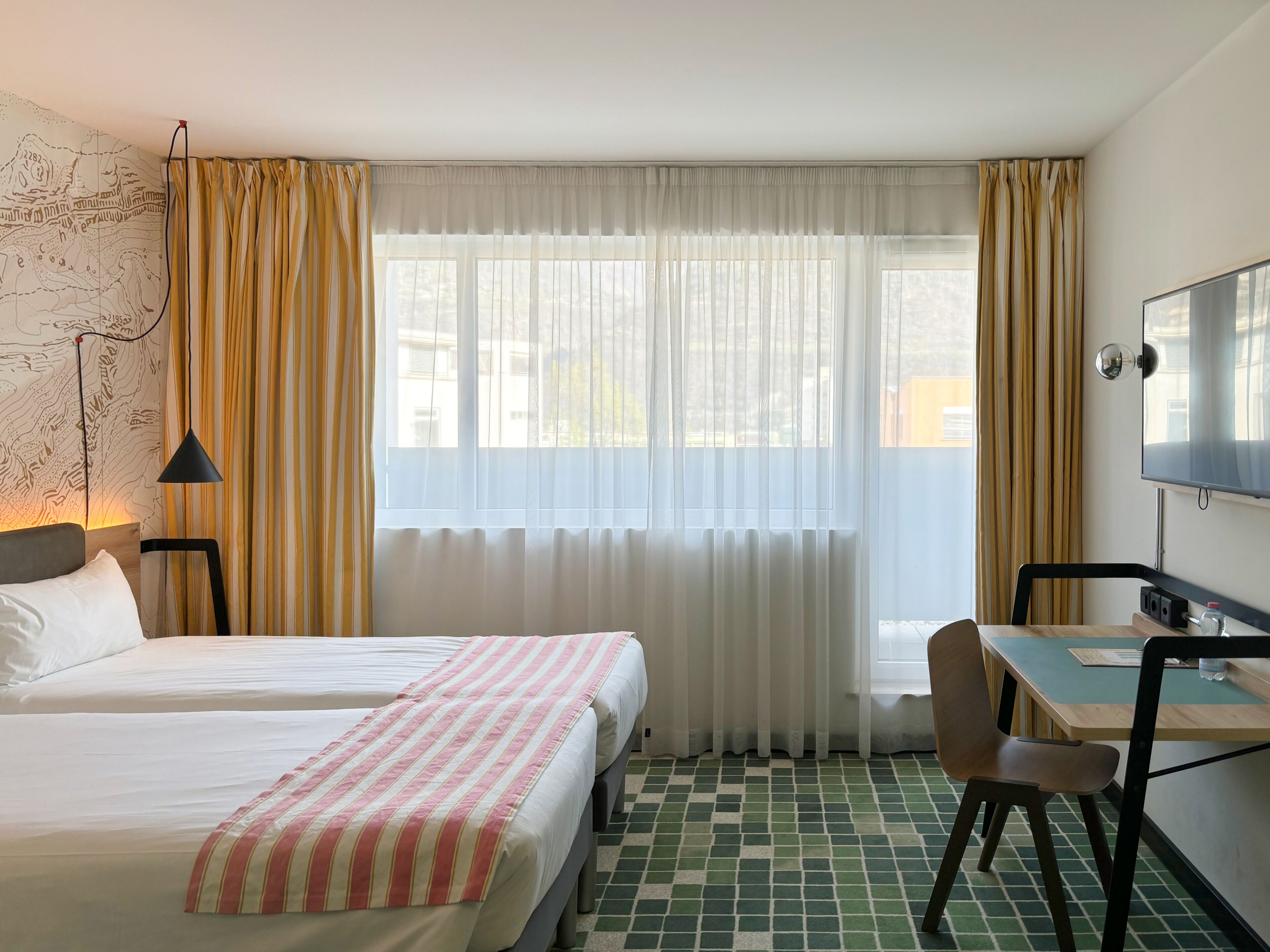 Een hotelkamer met twee bedden, een bureau met stoel, een televisie en een kaart aan de muur.