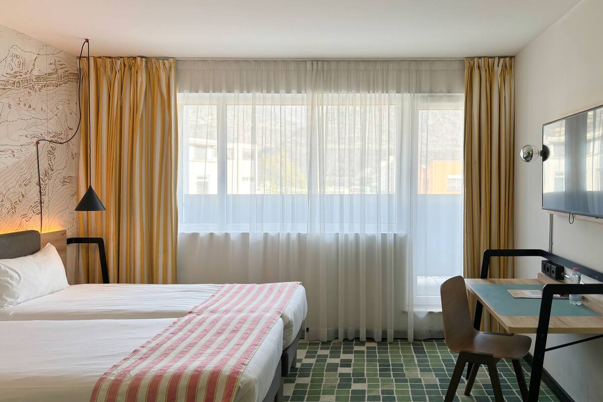 Habitación de hotel con dos camas, un escritorio con silla, un televisor y un mapa en la pared.