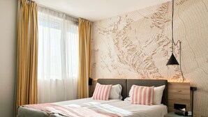 Uma cama de casal com roupa de cama listrada, uma mesa de cabeceira com abajur e uma parede com design de mapa topográfico.