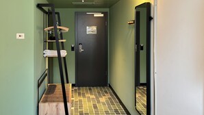 Um corredor estreito com escada de madeira, uma porta e um espelho.
