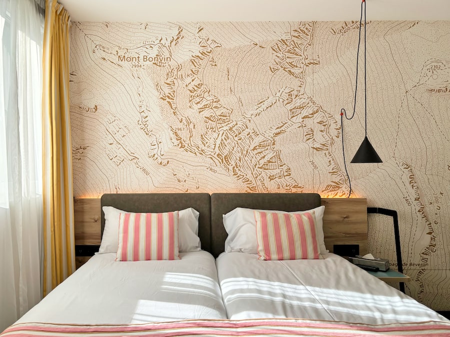 Cama doble con almohadas a rayas, cabecera de madera y papel tapiz con un mapa.