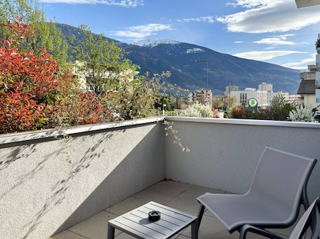 A balcony with a view of a mountain, a chair, and a small table.