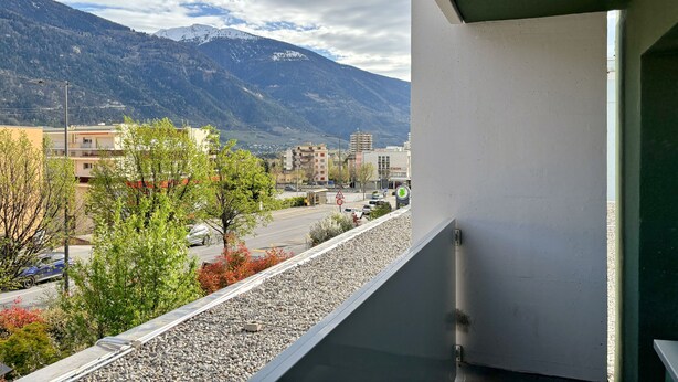 Uma varanda com vista para uma montanha, um estacionamento e edifícios ao fundo.