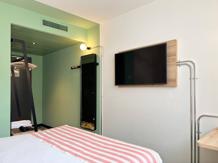 A bedroom with a bed, a mirror, a TV, and a shower area.