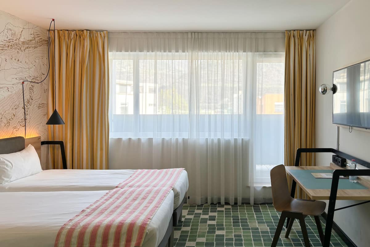 Habitación de hotel con dos camas, un escritorio con silla, un televisor y un mapa en la pared.