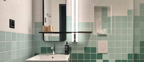 A modern bathroom with a white sink, a mirror, and a shelf with toiletries.