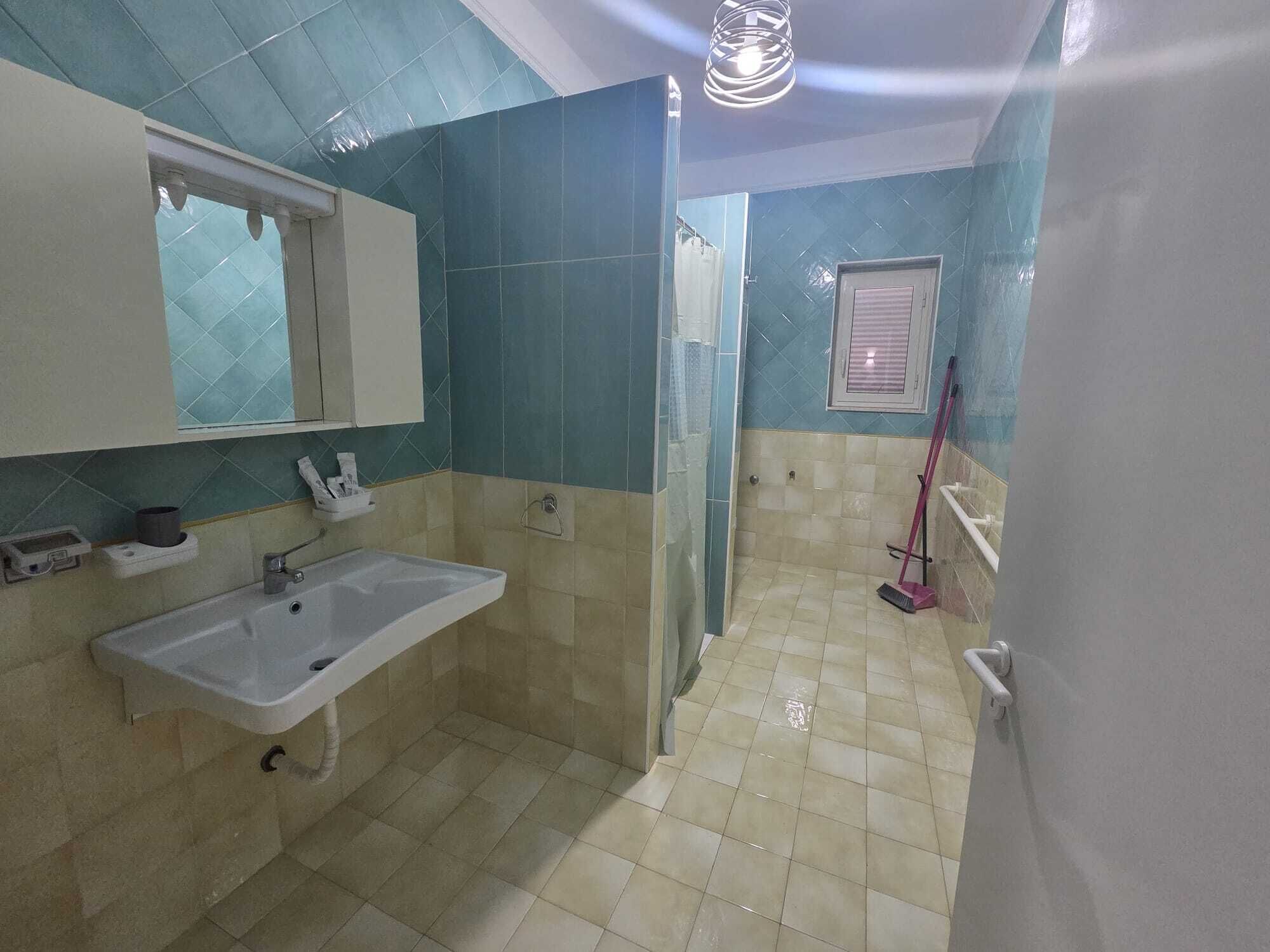 A bathroom with a sink, mirror, shower, and a mop.