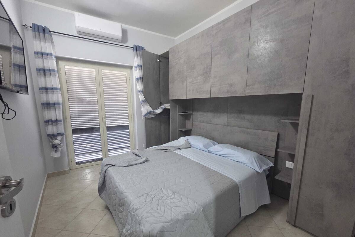 Une chambre à coucher avec un lit, une armoire, une fenêtre avec des rideaux et un sol carrelé.