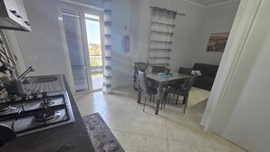 Cucina con piano cottura a gas, tavolo da pranzo con sedie, finestra con persiane e vista sull'esterno.