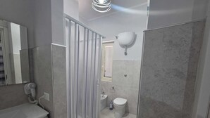 Un bagno con doccia, toilette, lavandino e asciugacapelli montato sulla parete.